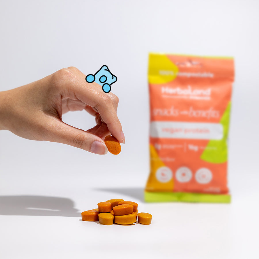 Person holding herbaland gummies with a pouch of vegan protein snacks with benefit gummies with tropical fruit flavor at the back