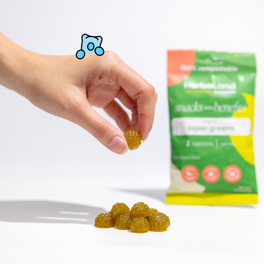 Person holding herbaland snacks with benefit gummies with a pouch of super green gummies with apple peach flavor in the back