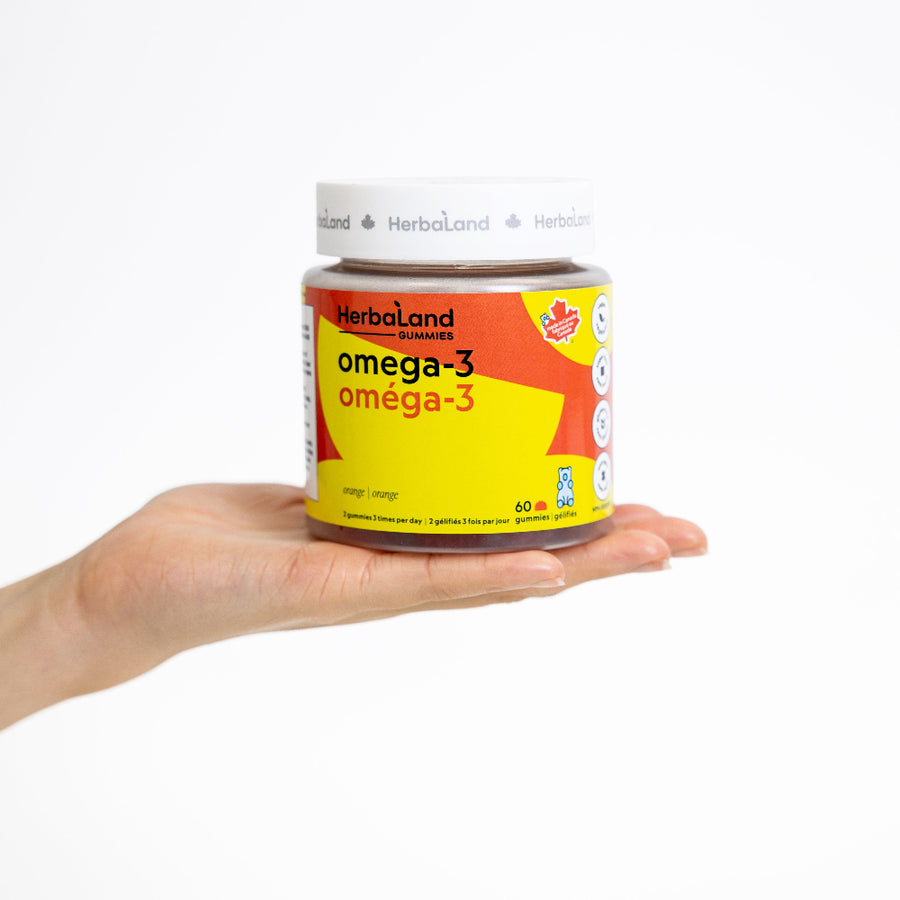 Hand holding a bottle of Herbaland omega-3 supplement on a white background