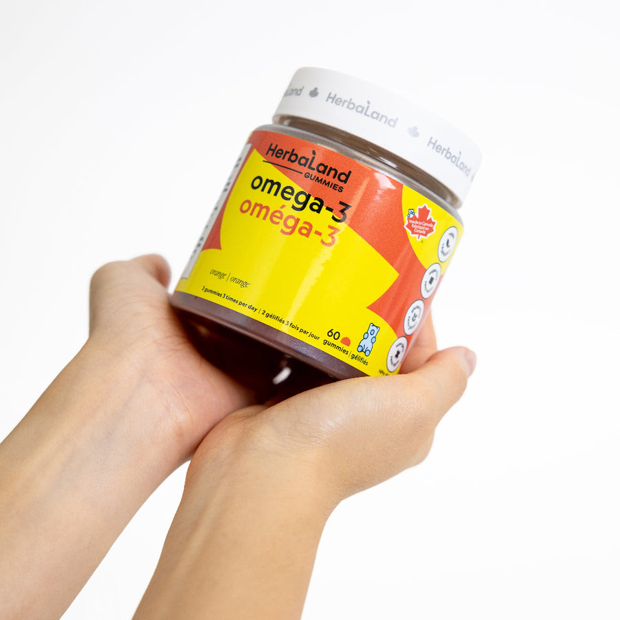 Hand holding a bottle of Herbaland omega-3 gummies on a white background